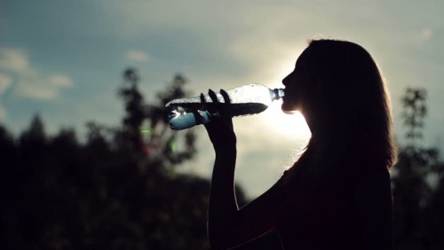 Woman drinking water over sunset