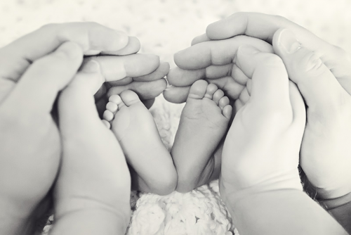 Newborn feet and parents' hands form a hear