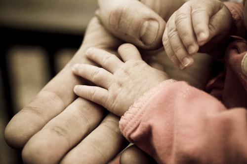 Photograph of a father holding his newborn daughter’s hand.